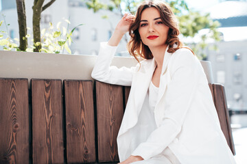 Young beautiful brunette woman wearing nice trendy white suit jacket. Sexy serious model posing in the street at sunny day. Fashionable female outdoors. Cheerful and happy. Evening makeup, sunglasses