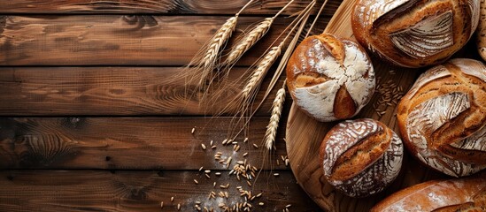 A rustic wooden board covered with a variety of whole grain bread loaves, scattered wheat ears, and space for text or images, representing a bakery theme. Copy space image
