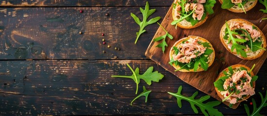 Poster - Top-view image of canned tuna toasts or sandwiches with lettuce and arugula on a dark wooden backdrop, offering ample copy space.
