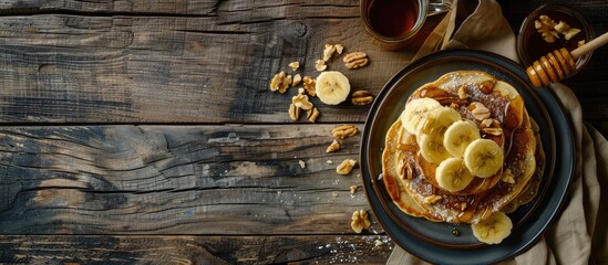 Dark wooden background sets the stage for a breakfast scene featuring homemade pancakes embellished with banana, nuts, and honey, along with a glass of coffee. Ample copy space image available.