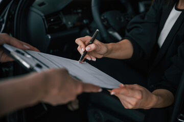 Process of buying new car, woman is signing documents while sitting in a new automobile