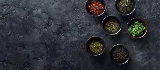 Aufkleber - Four bowls showcasing a variety of tea types, including black and green, set against a textured black stone backdrop with copy space image available.
