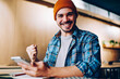 © BullRun - cheerful hipster guy in hat making yes gesture overjoyed with victory in online contest holding telephone, amazed young man celebrating achievement in passing exams successfully get message