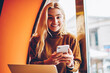 © BullRun - Portrait of cheerful hipster girl celebrating victory in online contest get email on smartphone, happy young woman excited popularity of publication in blog working on freelance in cafe on netbook
