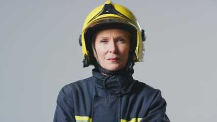 Wall Mural - Serious mature female firefighter wearing uniform holding helmet in front of plain studio background - shot in slow motion