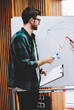 © BullRun - Smart young woman writing plan scheme on flipchart during training session conducting by successful male coach in university.Professional teacher checking graphic drawn on board by hipster student