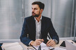© BullRun - Confident young entrepreneur in formal wear holding smartphone in hand while looking away and thinking on developing own corporate company.Thoughtful proud ceo pondering on solution working in office