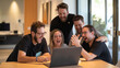© YURY YUTY - A group of colleagues celebrates a success while gathered around a laptop in an office.