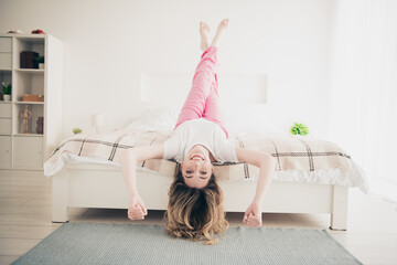 Canvas Print - Photo of positive girl lying bed upside down with fists smiling in white room