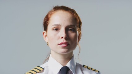 Wall Mural - Serious young female airline pilot or ship captain wearing uniform in front of plain studio background - shot in slow motion