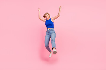 Wall Mural - Full size photo of pretty young woman jump raise fists empty space wear blue top isolated on pink color background