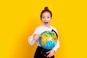 Poster - Photo of cute schoolgirl point finger world globe wear uniform isolated on yellow color background