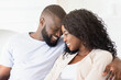 © Prostock-studio - A close-up shot of a couple smiling and looking at each other while sitting on a couch.