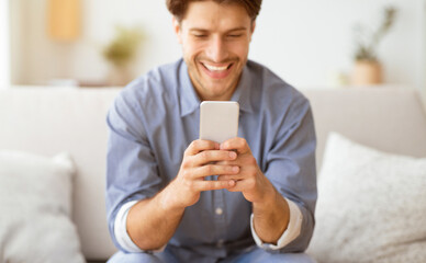 Poster - Happy Man Texting at Phone. Guy Playing On Smartphone Sitting On Sofa At Home