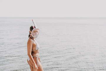 Wall Mural - A woman in a bikini stands on a beach with her face covered by a snorkel. Concept of adventure and excitement, as the woman is ready to explore the underwater world.