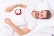 © be free - Morning wakeup. Sleepy man with alarm clock while lying in bed. Morning awakening. Sleepy man turning off alarm clock. Waking up early. Time to wakeup and get up. Lazy Sunday