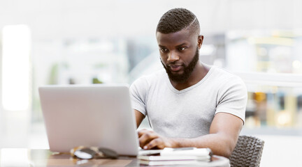Poster - A man works on a laptop in a cafe setting, focusing on his task.