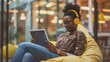 © The Little Hut - Creative intern browsing online with a tablet listening to music on wireless headphones Female on a break sitting on bean bags in a casual office space to improve creativity work and m : Generative AI