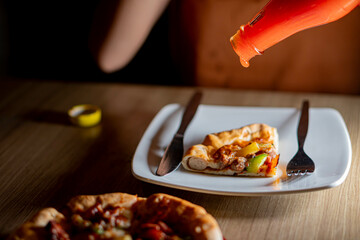 Pouring ketchup on pizza slice