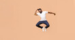 © Prostock-studio - African American young man is jumping in the air with excitement. He is wearing a white t-shirt and blue jeans. The background is a soft peach color