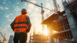 © Curioso.Photography - Construction worker in safety vest observing a building site at sunrise.