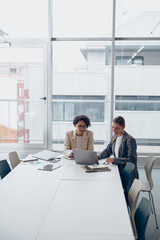 two focused female coworkers working on project together and use laptop sitting in office