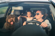 © Soloviova Liudmyla - Smiling woman driving car with  brown Maltipoo dog and her daughter in backseat, enjoying sunny day. Image captures joyful family moment during road trip, highlighting happiness and togetherness