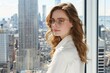 © ProPhotos - A woman with glasses and a white shirt stands in front of a window overlooking a city skyline.