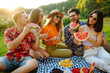 © maxbelchenko - Young cheerful friends happy positive smile eat fruit watermelon party countryside outdoors. Foods, travel, nature and picnic concept