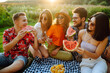 © maxbelchenko - Young cheerful friends happy positive smile eat fruit watermelon party countryside outdoors. Foods, travel, nature and picnic concept