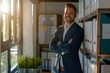 © neatlynatly - A middle-aged business man is standing in an office, smiling confidently with arms crossed. The background includes shelves with binders and a sunlit window.