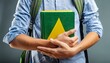 © Rmcarvalhobsb - Um estudante de mochilas segurando um livro com a capa nas cores verde e amarelo. Cores em referência ao Brasil. Isolado no fundo cinza. Educação, Ensino, Brasileiro.