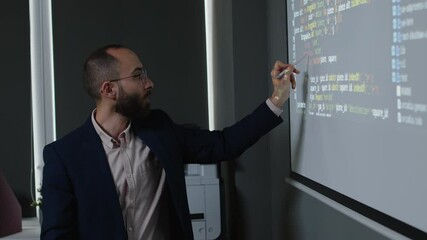 Medium side shot of young nerdy male programming teacher circling code variables on projector screen, explaining purpose, while giving software development lesson in college