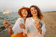 © maxbelchenko - The sparklers in the hands of young women on the beach. Happy women walking with sparkler fireworks on beach. Summer holidays, party, vacation, relax and lifestyle concept.