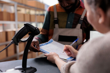 Wall Mural - Diverse team analyzing merchandise checklist signing report in warehouse, discussing products quality control. African american employee wearing industrial overall, working at clients orders. Close up