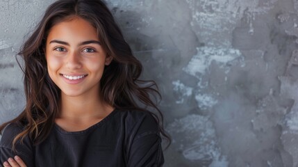 Wall Mural - A young Hispanic woman with long brown hair smiles confidently while standing in front of a grey wall, arms crossed. Generative AI