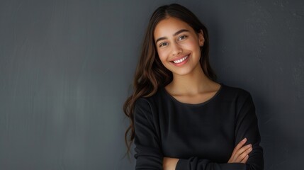 Wall Mural - A young Hispanic woman with long brown hair smiles warmly at the camera with her arms crossed, standing against a grey wall. Generative AI