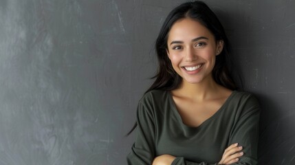 Wall Mural - A portrait of a young Hispanic woman with long black hair and a warm smile. She is standing against a grey wall with her arms crossed, looking directly at the camera. Generative AI