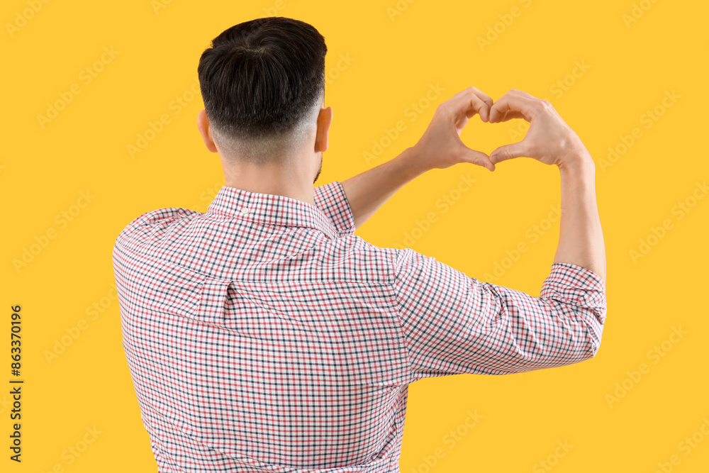 Handsome man making heart with his hands on yellow background, back view