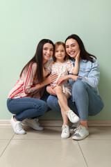 Canvas Print - Young lesbian couple with adopted little girl hugging near green wall