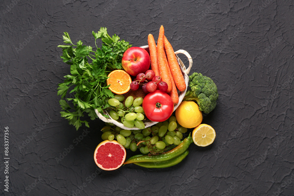 Wicker basket with different fresh fruits and vegetables on black background