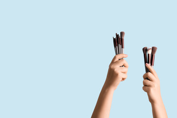 Wall Mural - Female hands with makeup brushes on blue background