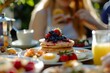 © GreenOptix - Woman eating pancakes with blueberry jam and fruit on top, surrounded by other dishes such as eggs, bacon, bagels, smoothies, juice, outdoor cafe table