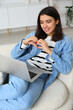 © Pixel-Shot - Young woman with laptop making heart gesture on online date at home