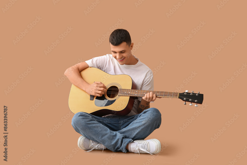Handsome young man playing guitar on beige background