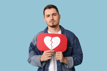 handsome young displeased man with heart dislike icon on blue background