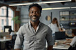 © btiger - Confident African American businessman in casual attire smiling in modern tech office with team working behind