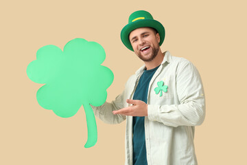 Wall Mural - Happy young man in leprechaun's hat showing clover on beige background. St. Patrick's Day celebration