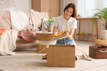 Wall Mural - Young pretty woman folding clothes in donation cardboard box at home