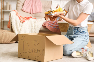 Young pretty woman folding baby clothes in donation cardboard box at home